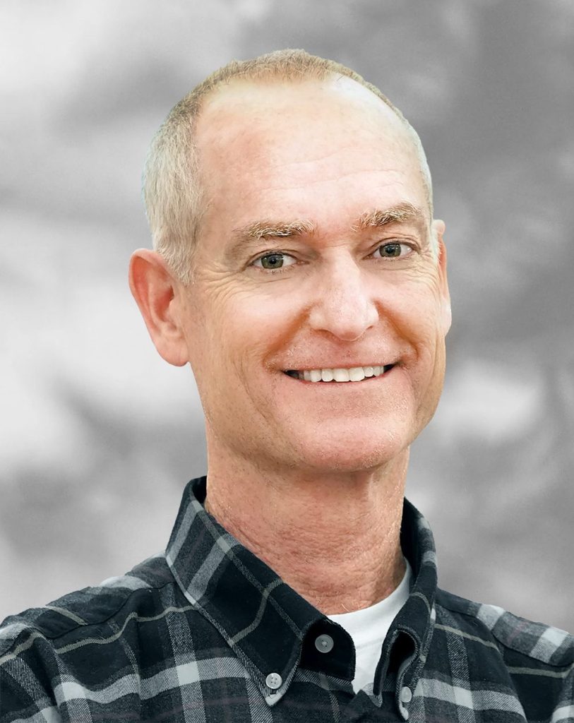 A portrait of of Walt Cecka, a smiling man with short hair wearing a plaid shirt against a blurred background.