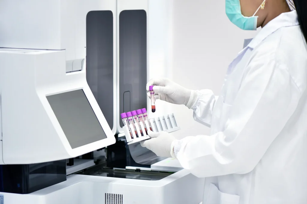 A lab technician in a white coat holds blood samples near laboratory equipment, showcasing the legacy IVD product modernization process while ensuring 510(k) compliance.