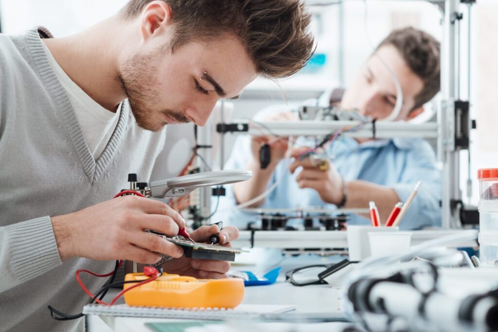 Triple Ring work with electronic components and tools at a desk, focusing on assembling or repairing devices, with various equipment and wires visible.