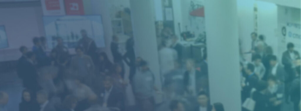 A group of people are gathered in a large indoor space, possibly attending the US/Japan Reverse Pitch Event, with informational displays and booths visible in the background.