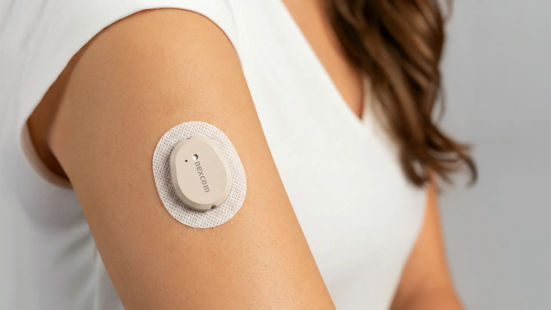 A person wearing a white shirt has a Dexcom glucose monitoring device attached to their upper arm.