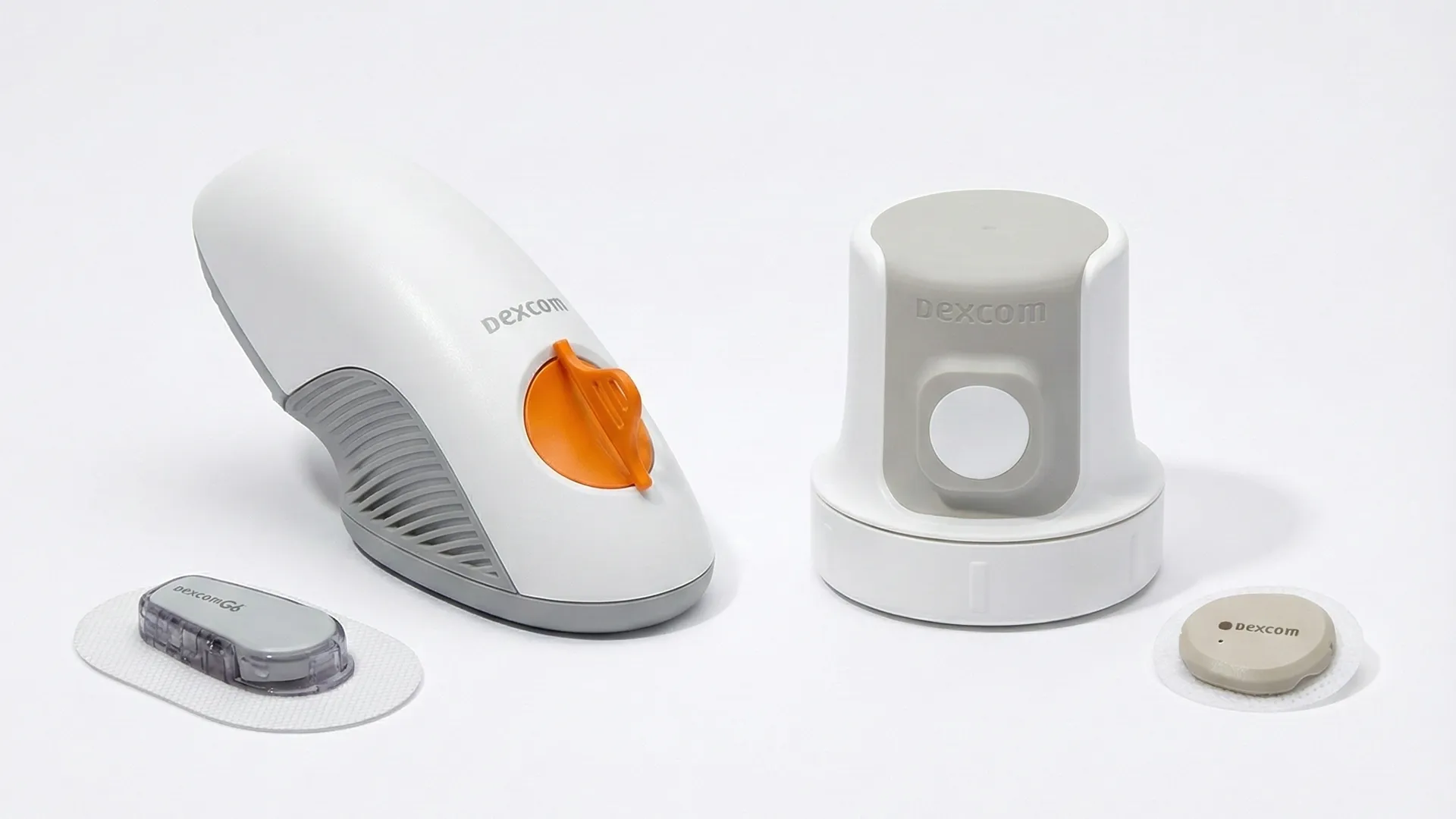 Dexcom glucose monitoring devices and applicators are arranged on a white surface, including sensors, a transmitter, and insertion tools.
