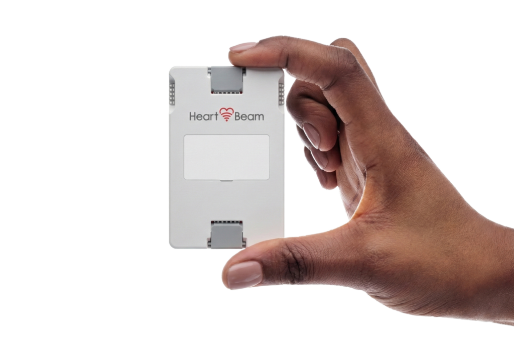 A hand holds a small rectangular medical device labeled "Heart Beam" against a plain white background.