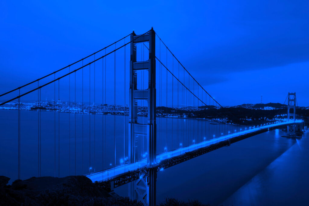 The Golden Gate Bridge spans across the water with city lights in the background, shown under a blue color filter, symbolizing the spirit of Innovation Diplomacy connecting people and ideas.