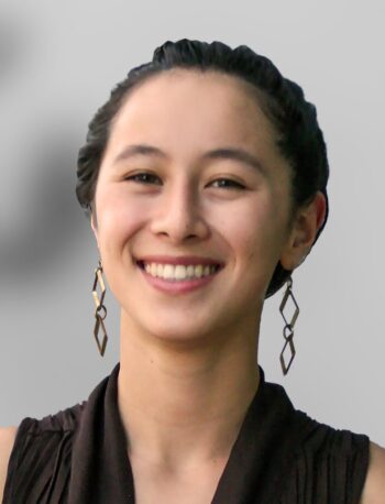 A photo of Amanda Powell, a woman with dark hair pulled back, wearing geometric earrings and a sleeveless dark top, smiling at the camera against a plain gray background.