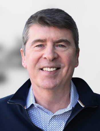A middle-aged man with short brown hair, Lee McGrath brings more than twenty years of financial leadership experience to his role as Chief Financial Officer, smiling at the camera in a dark jacket over a patterned shirt against a plain light background.