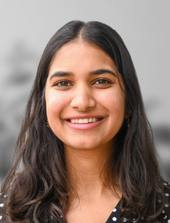 A photo of Shreya Jindal, a woman with long dark hair and a black polka dot top smiling at the camera against a neutral, blurred background.