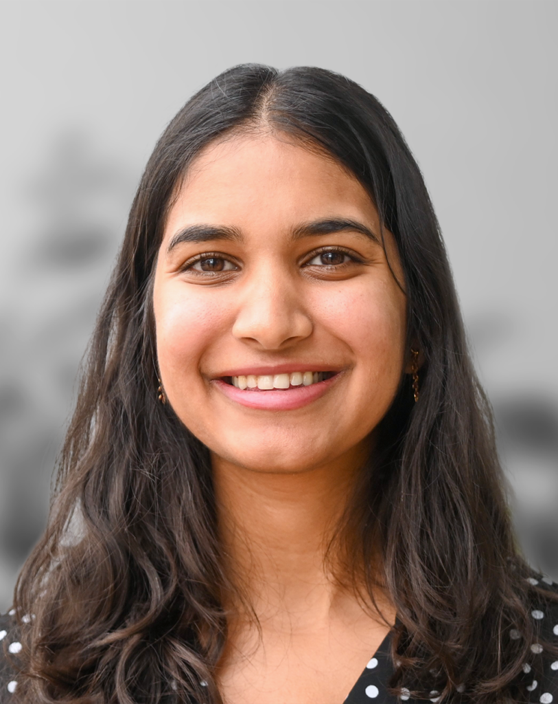 A photo of Shreya Jindal, a woman with long dark hair and a black polka dot top smiling at the camera against a neutral, blurred background.