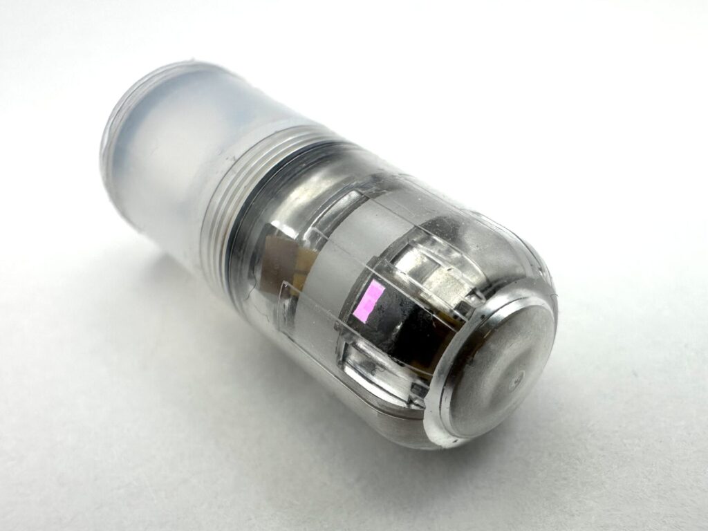 A transparent plastic capsule with internal electronic components is shown on a plain white background.