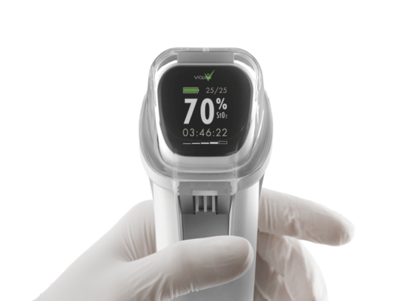 Gloved hand holding a medical device displaying 70% SpO2, 25/25, and a timer reading 03:46:22 on its digital screen.